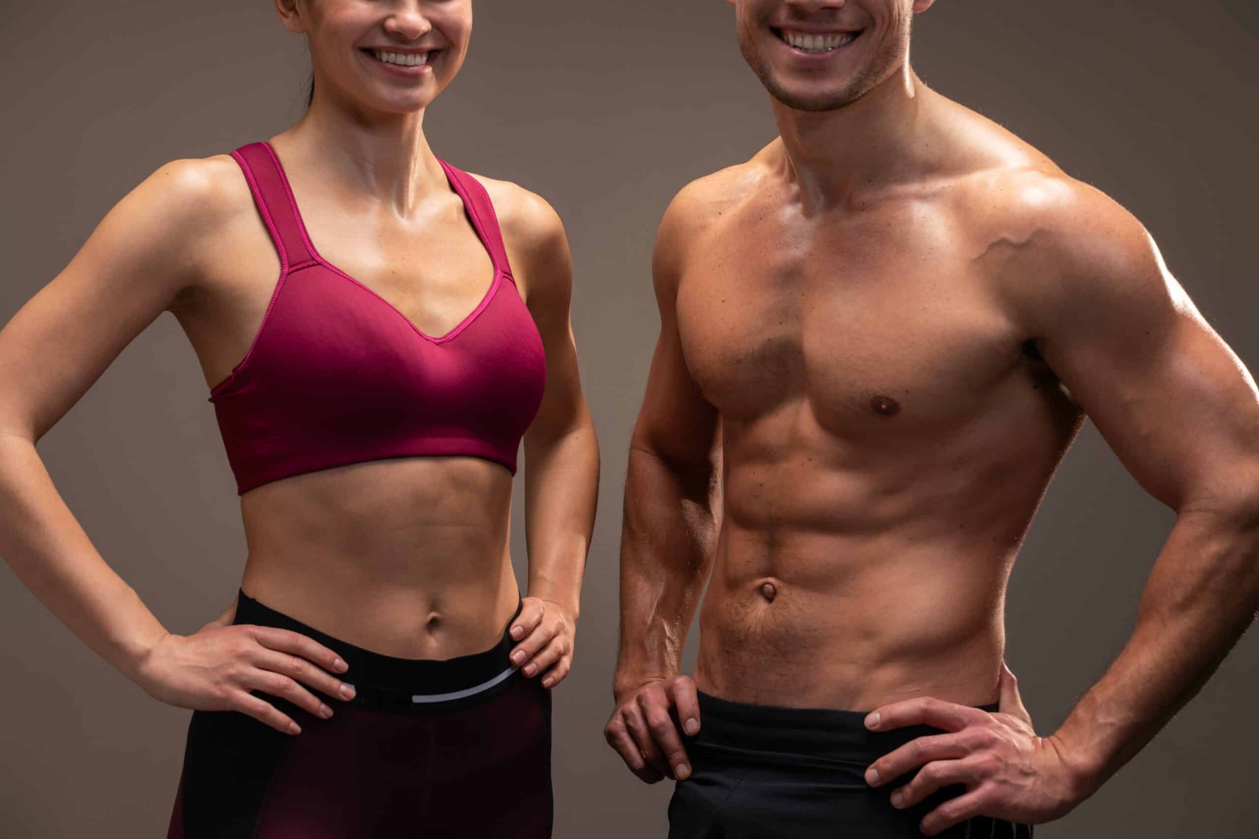 Cropped view of the athletic man and woman posing to the camera before fitness exercise at the studio with brown wall