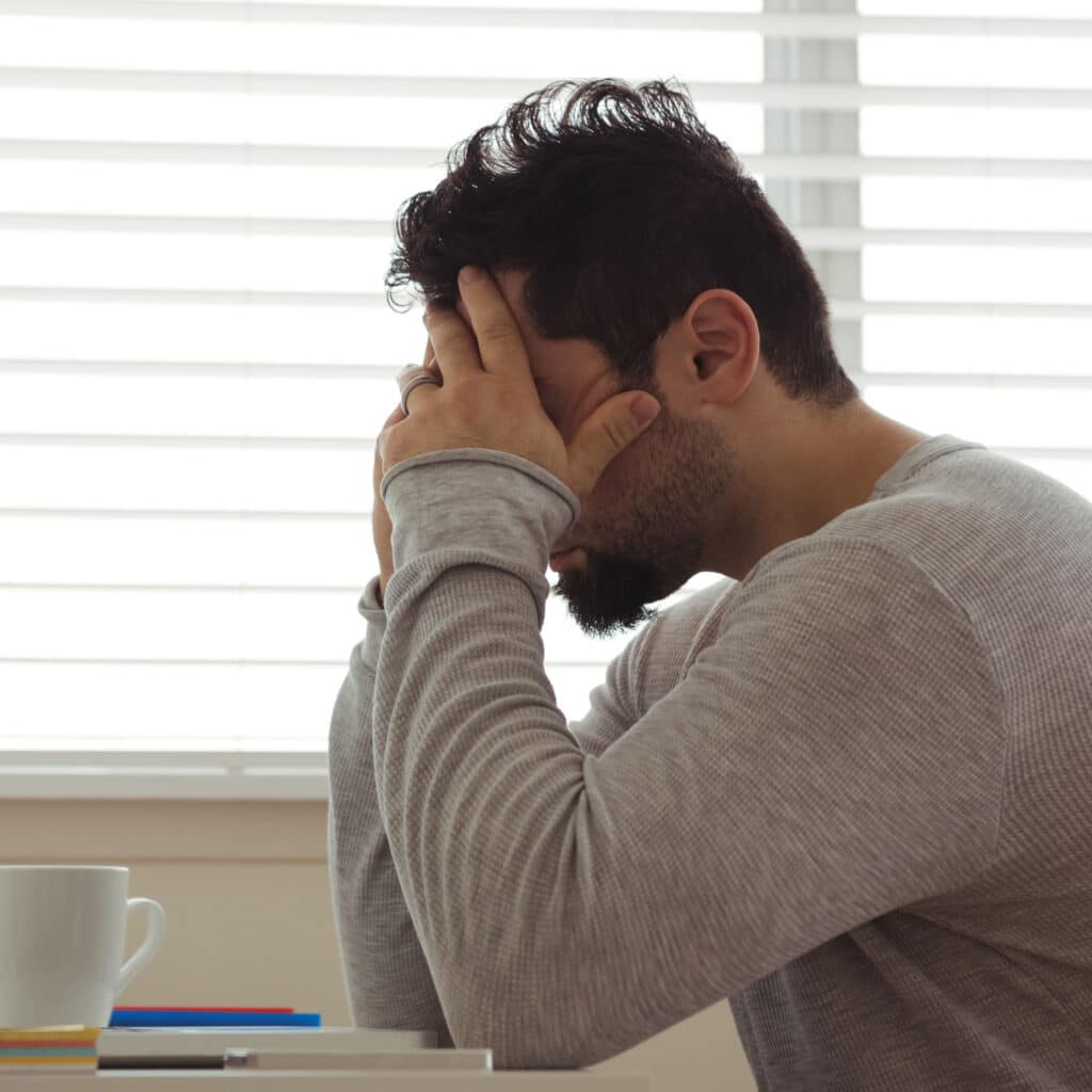 Stressed man sitting with hands on head at home