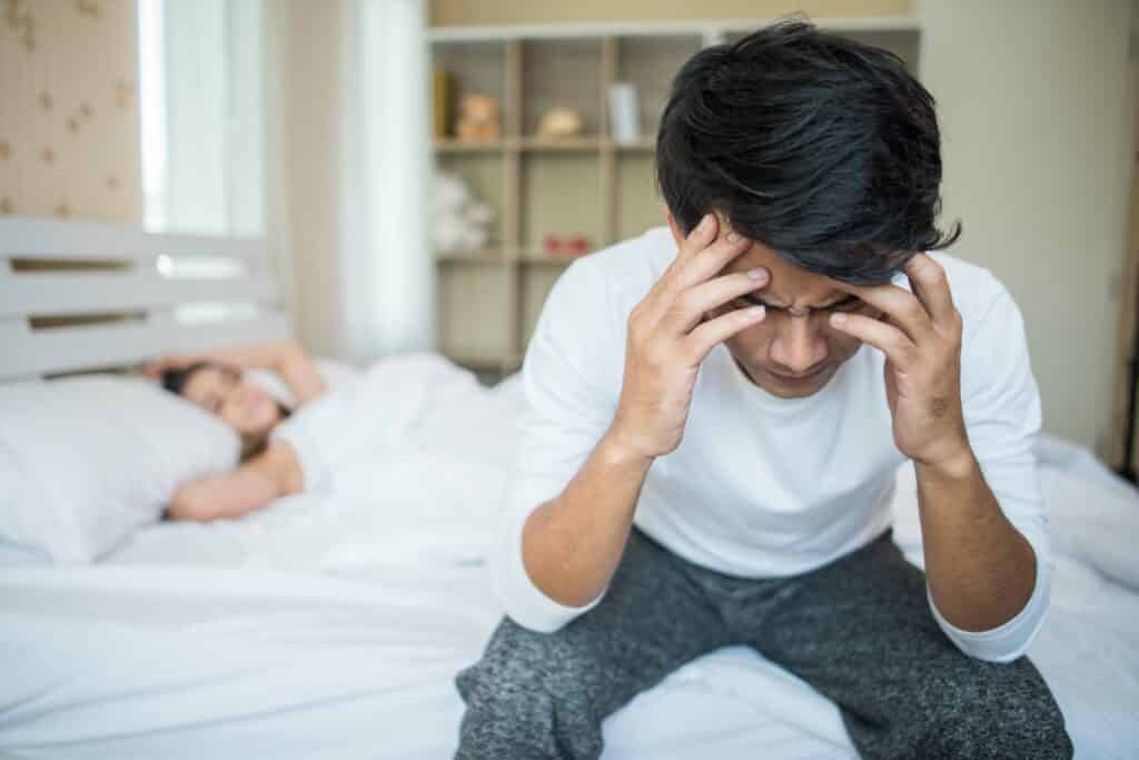 Upset man having problem sitting on the bed after arguing with h