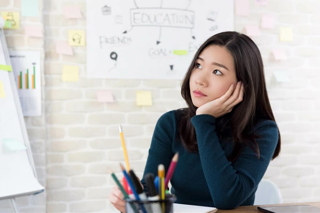 Asian female college student thinking with hand on cheek