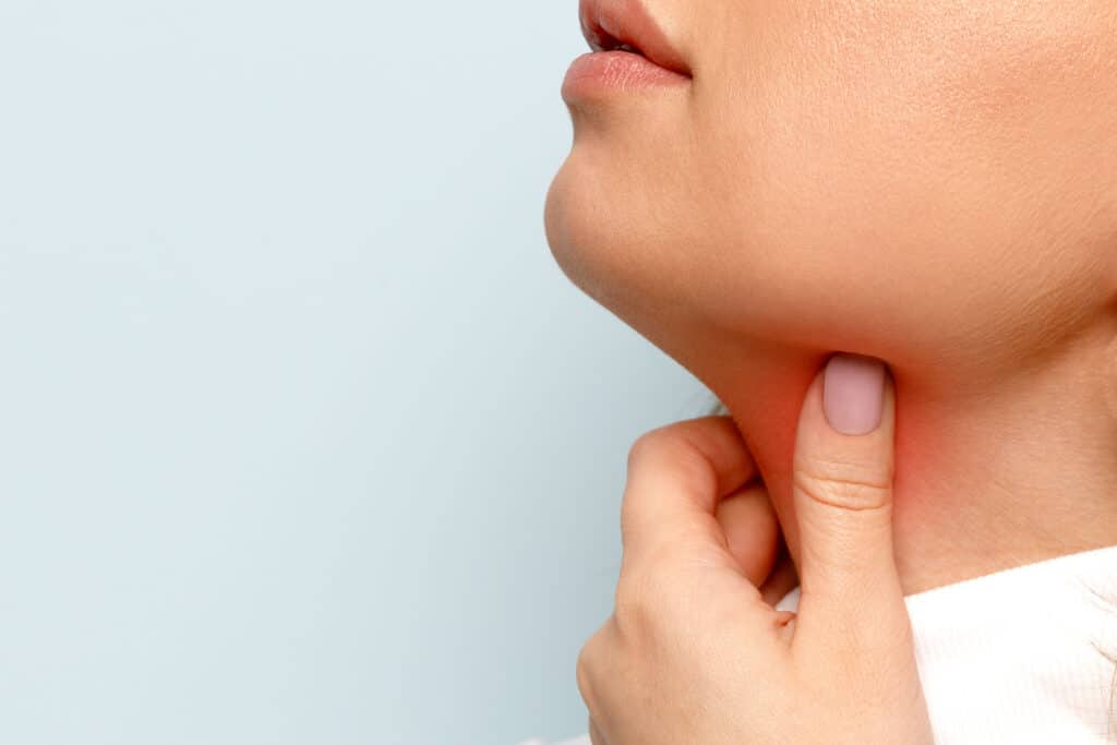 woman touches fingers of sore throat, isolated on blue backgroun