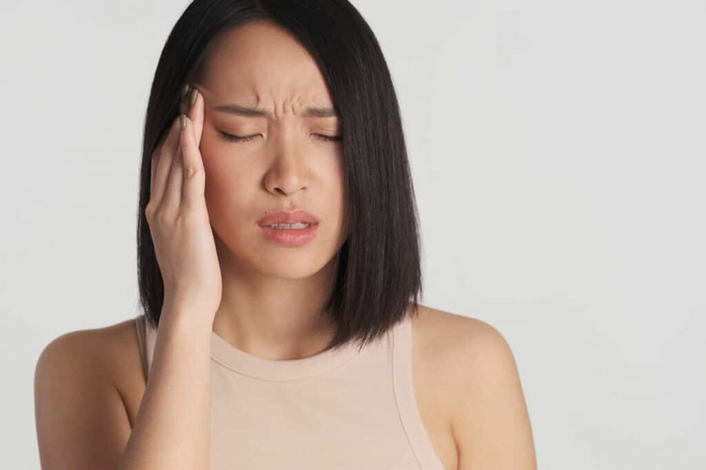 Asian keeping fingers on temples suffering from headache over wh