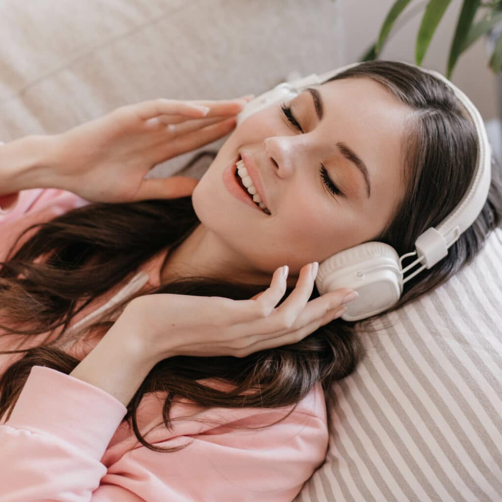 Young girl puts on her massive headphones and relaxes on sofa in cozy apartment